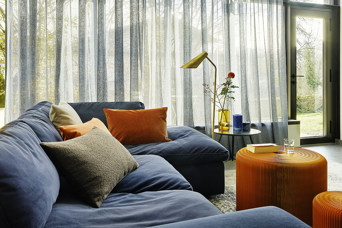 Wohnzimmer mit gemütlicher Couch und großem leicht transparenten Vorhang